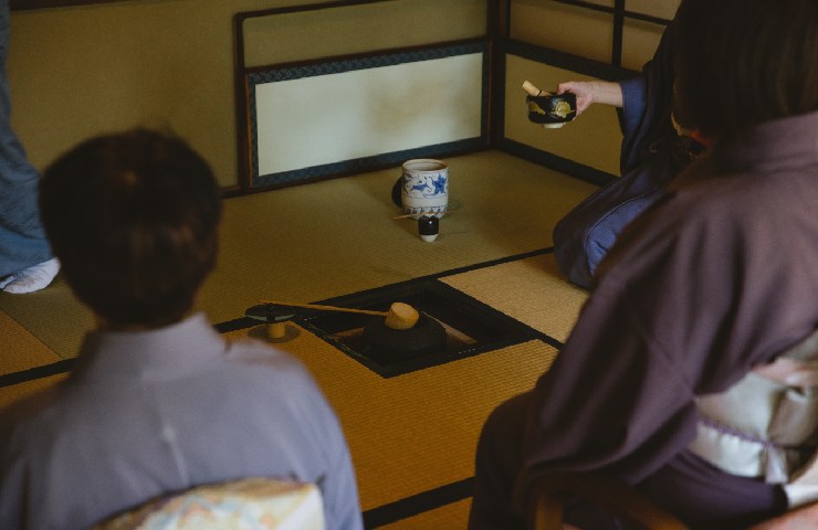 Persone sedute sul tatami che fanno la cerimonia del té giapponese vestite con dei kimoni da interno