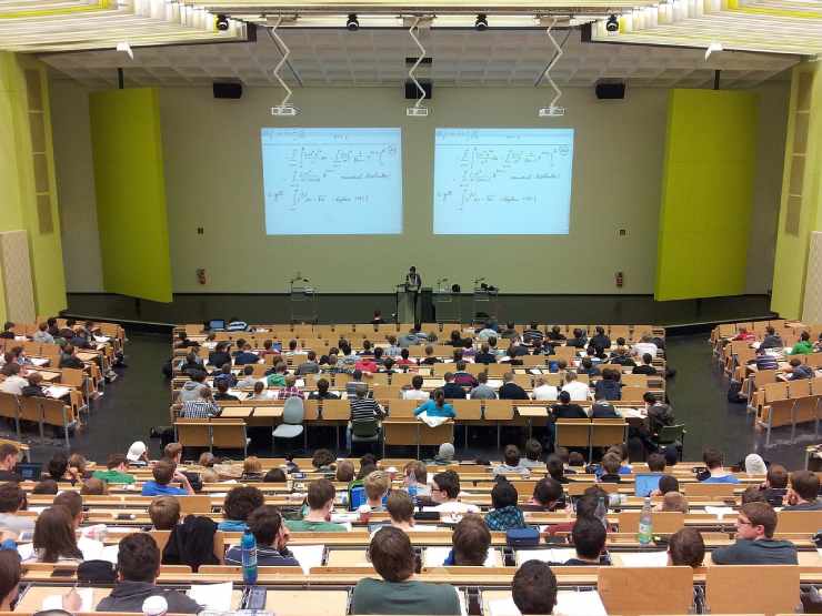 Aula universitaria con studenti ai banchi e slide proiettate al muro