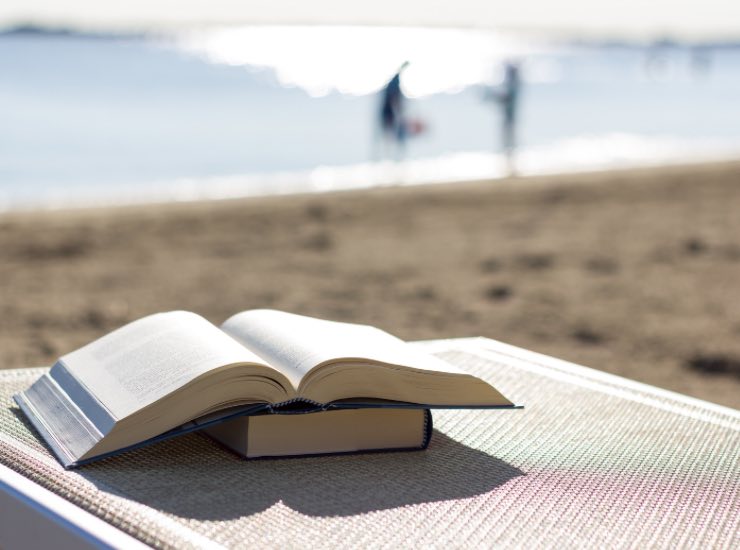 Libri appoggiati su un telo con sfondo la spiaggia