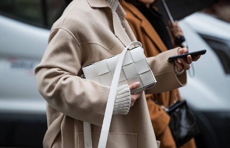 Una borsa di pelle bianca di un grande marchio tenuta da una donna con cappotto beige